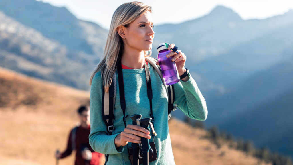 Woman hiker taking a water break on a mountain trail, an important step to prevent altitude sickness during an Andean trek - Authentic Incan Adventures